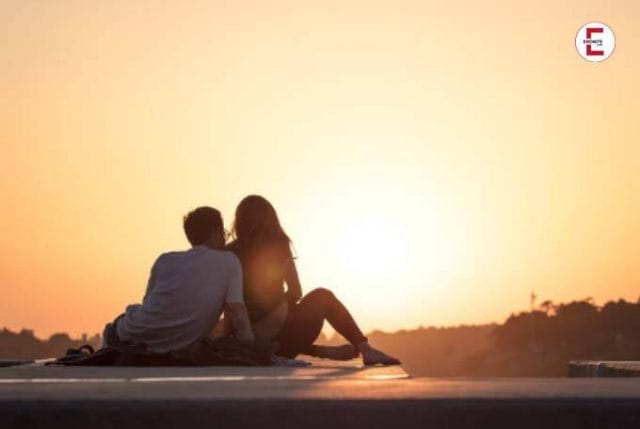 Verliebtes Paar sitzt zusammen auf einer Straße und beobachtet einen Sonnenuntergang