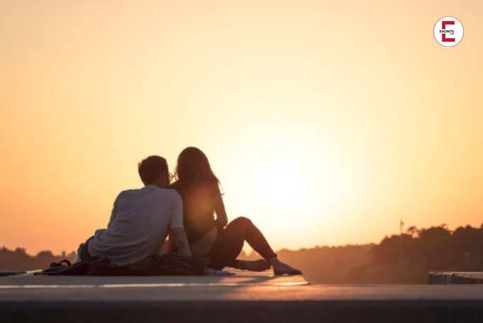 Verliebtes Paar sitzt zusammen auf einer Straße und beobachtet einen Sonnenuntergang